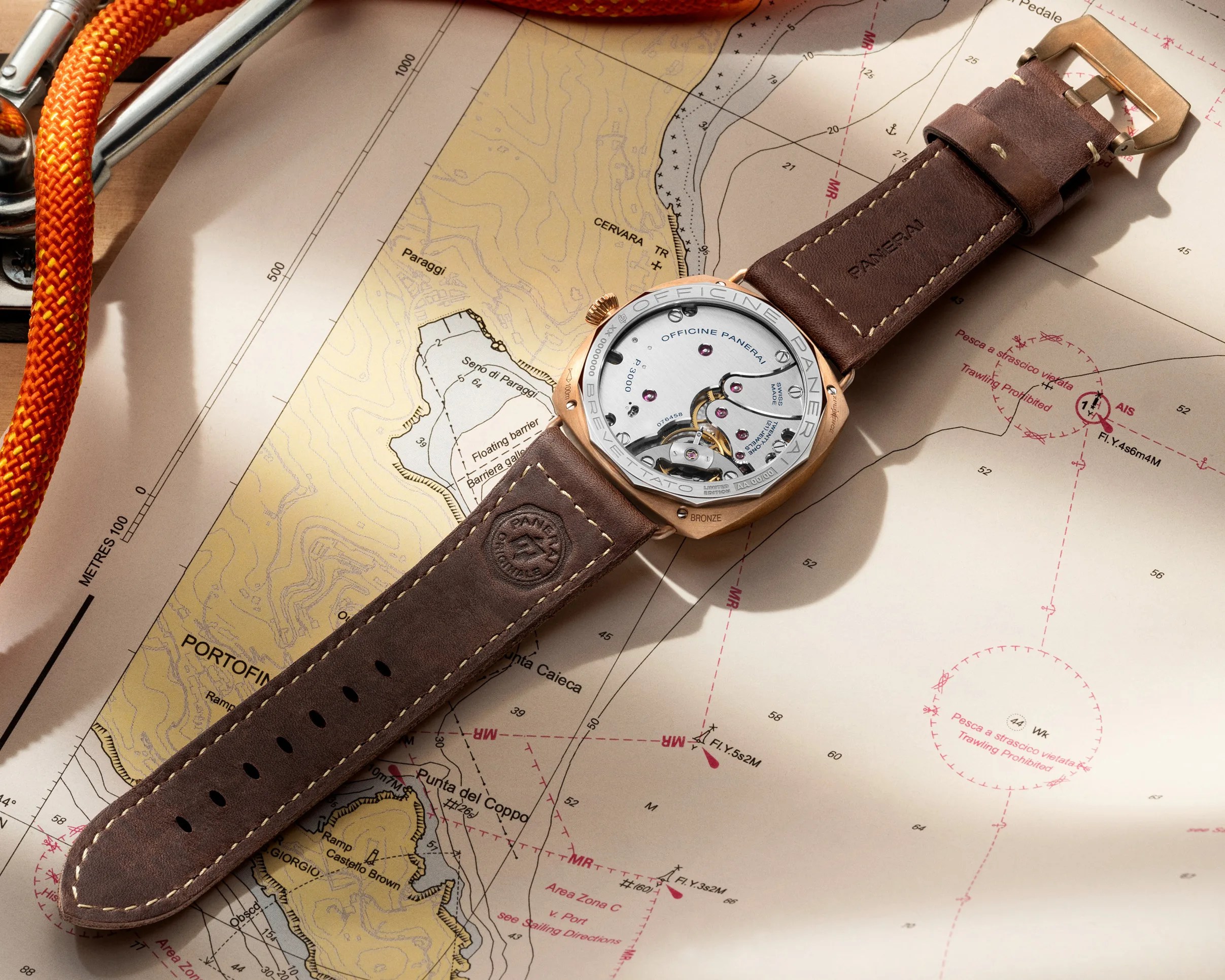 Bronze Panerai wristwatch with visible mechanical movement and brown leather strap on a nautical map.
