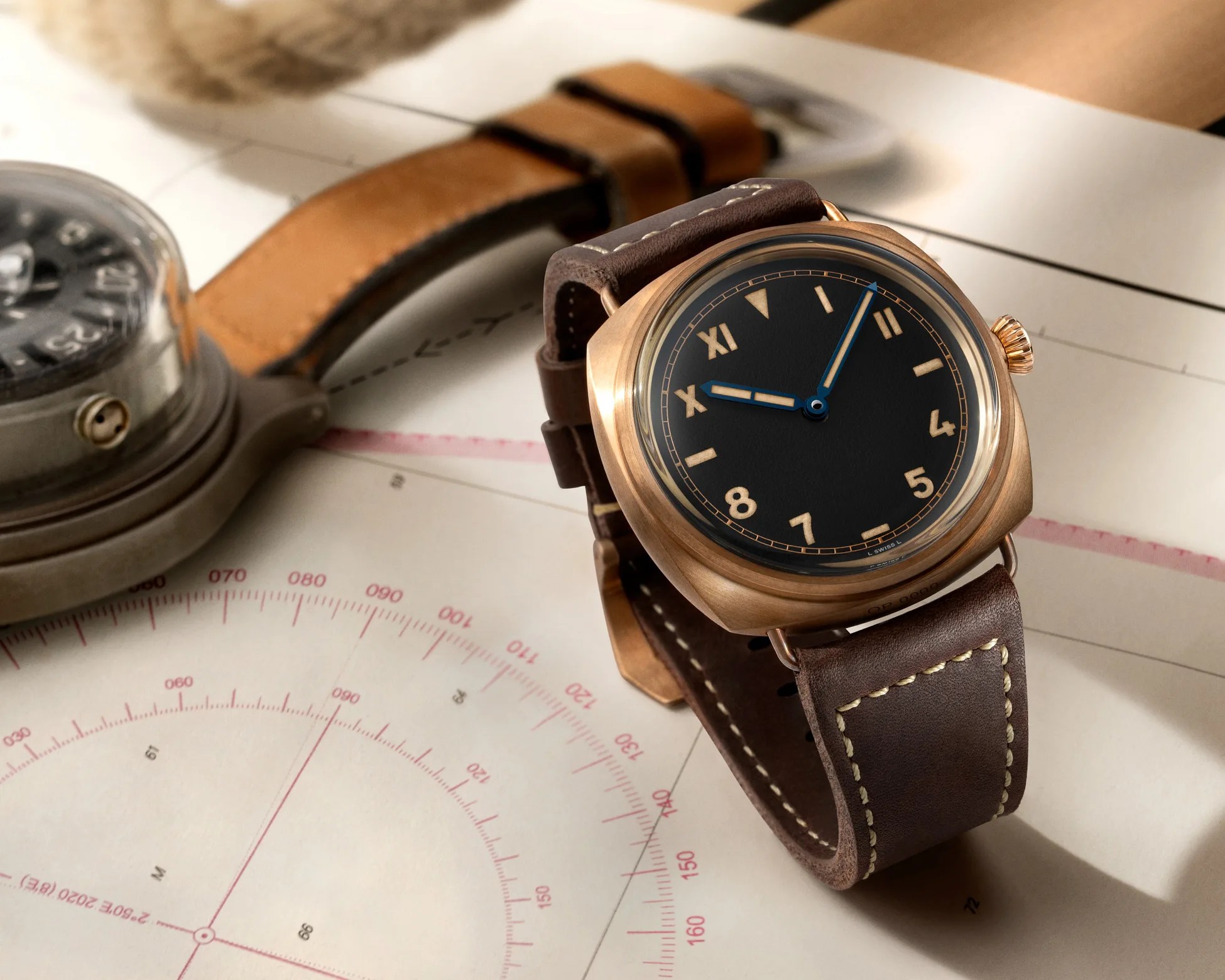 Bronze wristwatch with black dial, gold numerals, blue hands, and brown leather strap with beige stitching.