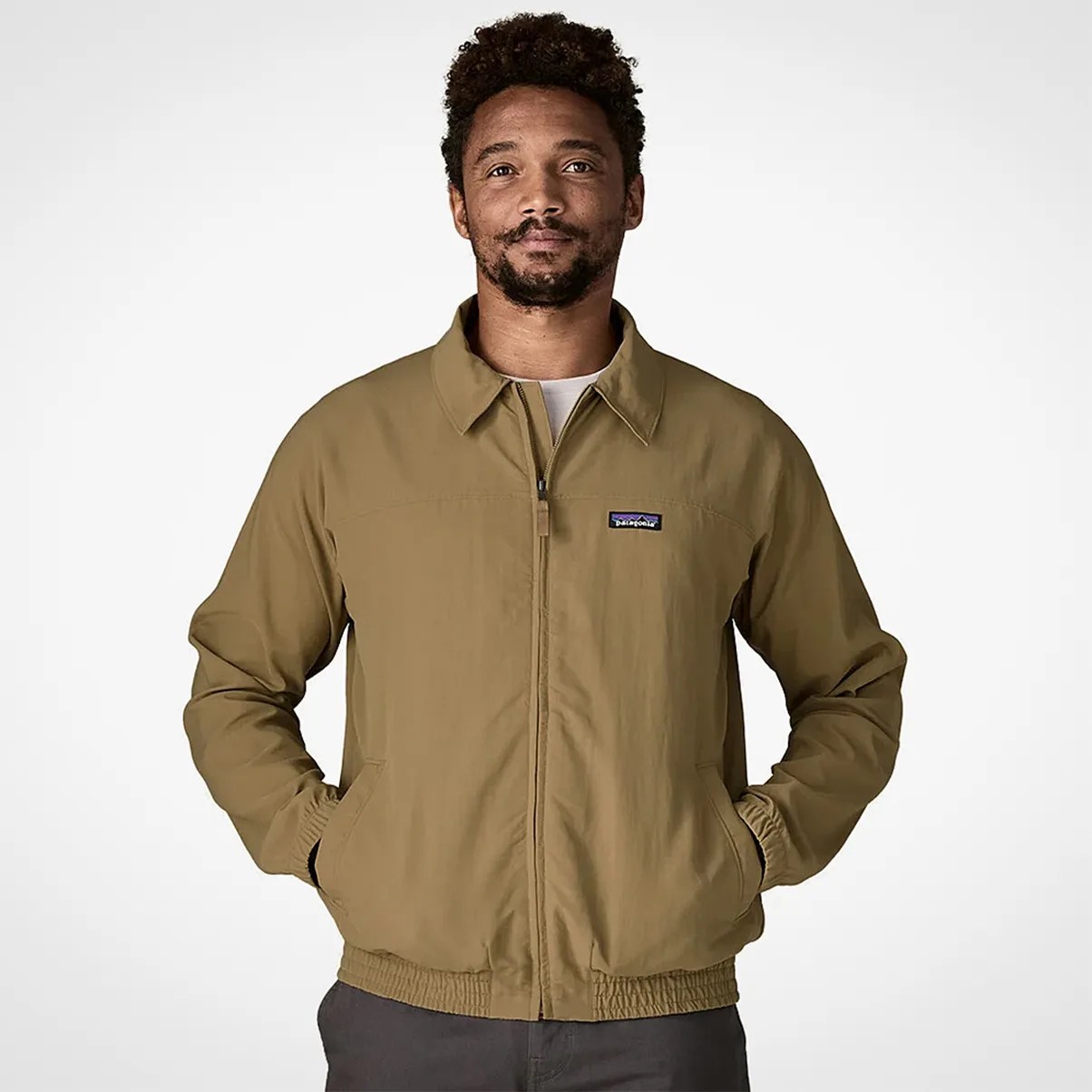 Man wearing a tan zip-up jacket with elastic cuffs and hem, featuring a small Patagonia logo on the chest.