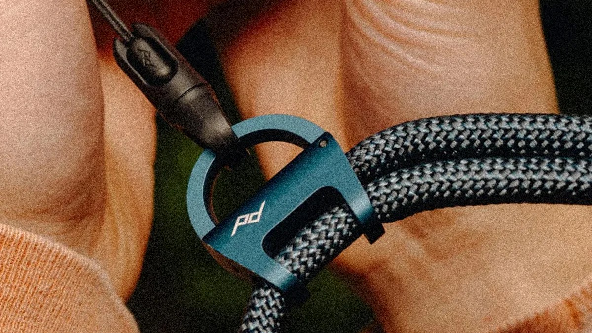 Blue metal rope tensioner with "pd" logo securing a black and gray braided rope held by a person.