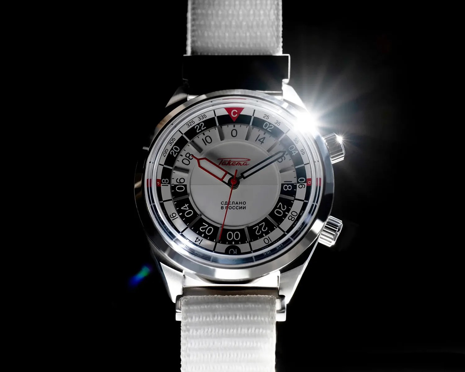 Silver wristwatch with white dial, black and white 24-hour markings, red and black hands, and white fabric strap.