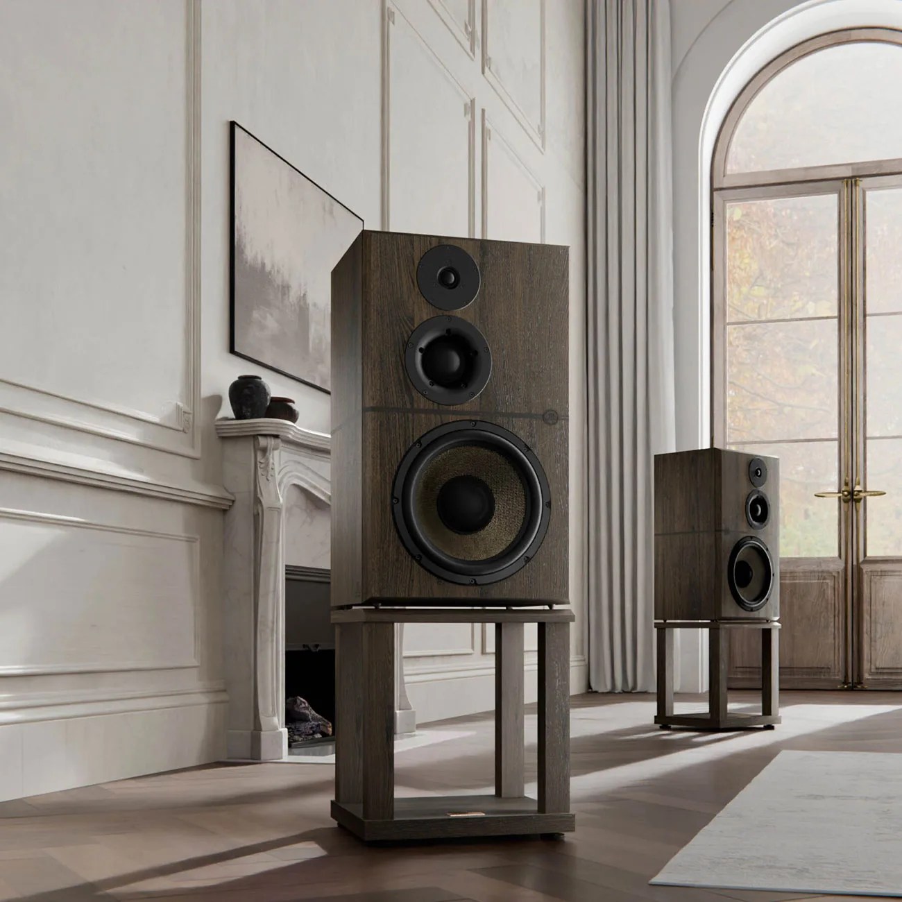 Pair of large wooden floor-standing speakers with black drivers in a bright room with a fireplace and arched window.