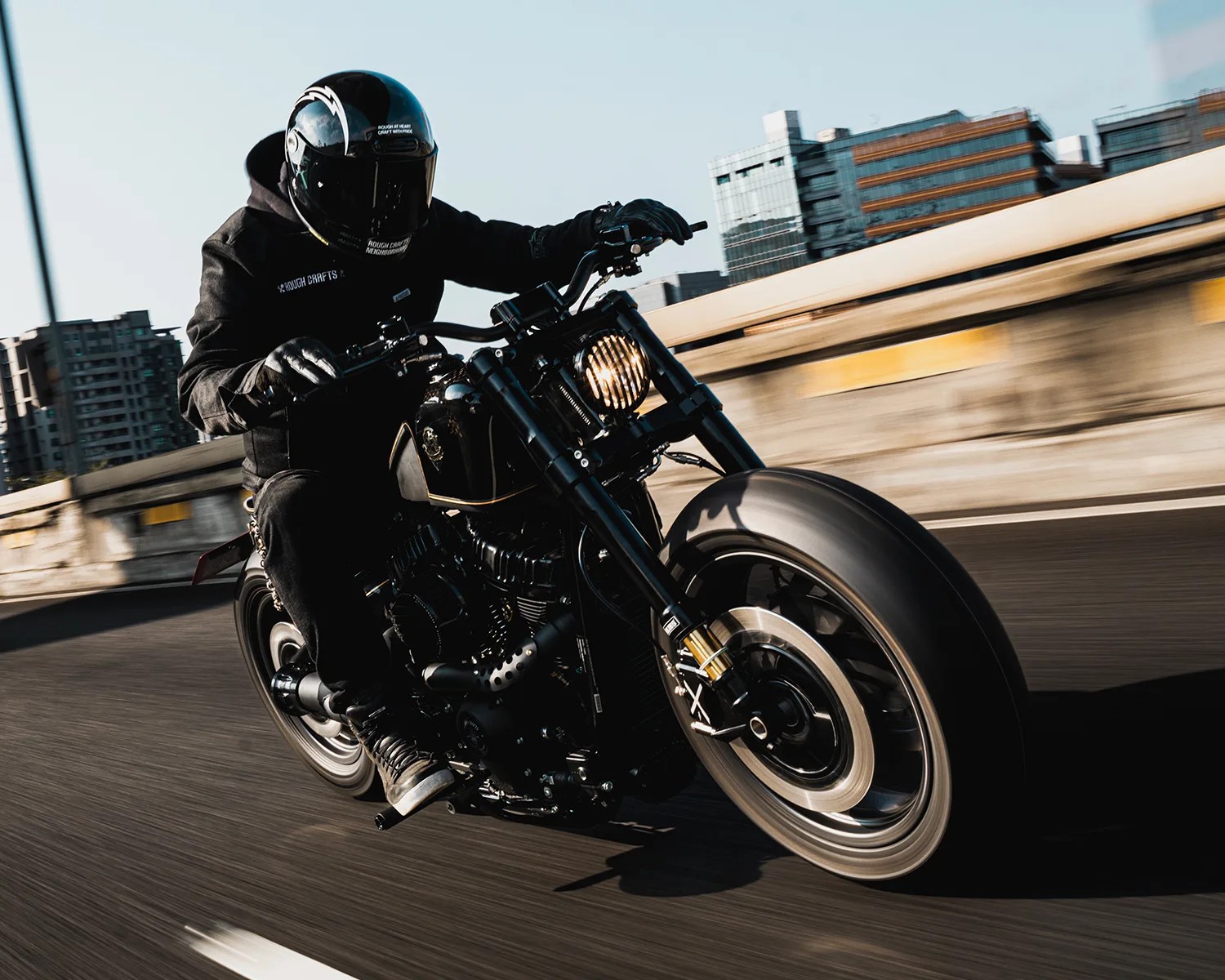 Person wearing black helmet and gloves riding a black motorcycle on a city road.