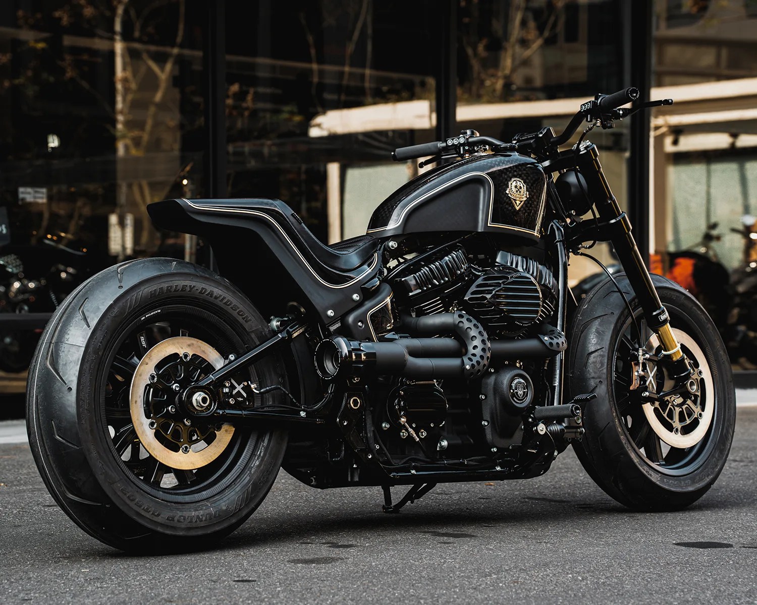 Black custom Harley-Davidson motorcycle with wide rear tire and gold-accented tank parked on street.