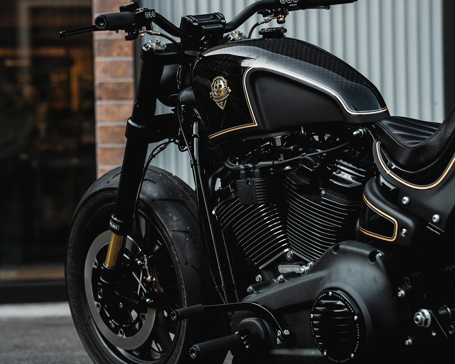 Close-up of a black motorcycle engine and fuel tank with gold trim and a leather seat.