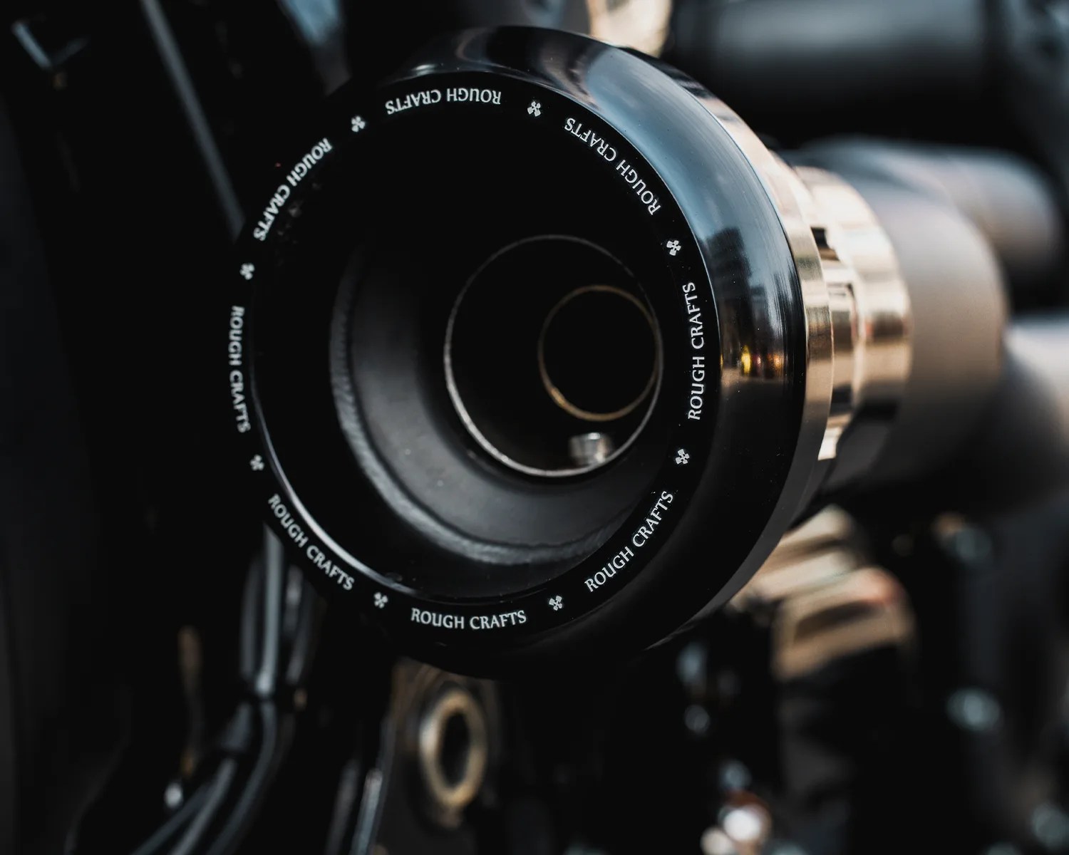 Close-up of a black and metallic motorcycle exhaust tip with "ROUGH CRAFTS" text around the edge.