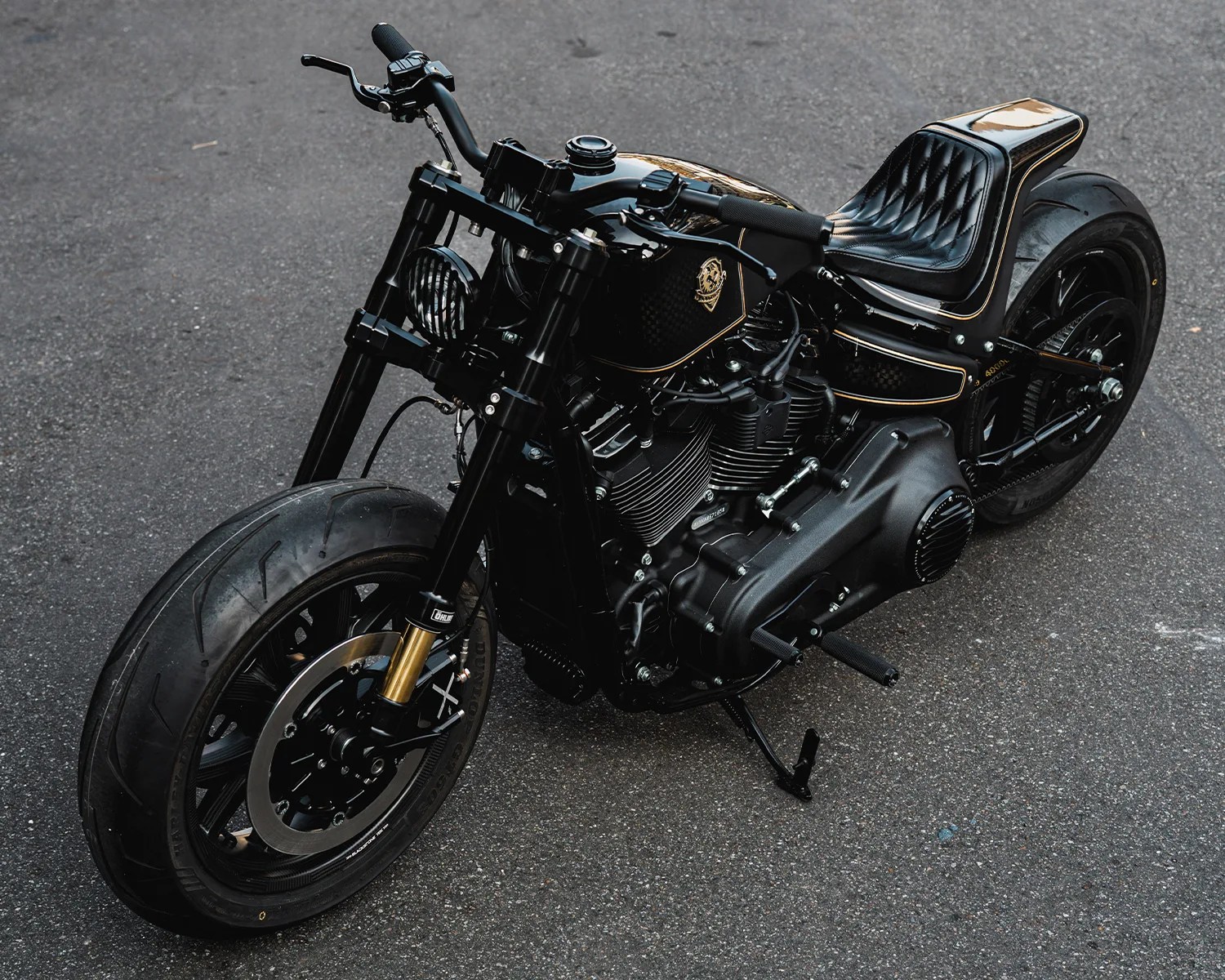 Black custom motorcycle with gold pinstriping and quilted leather seat parked on asphalt.