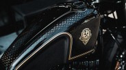 Glossy black motorcycle fuel tank with gold trim and a metallic emblem on the side.