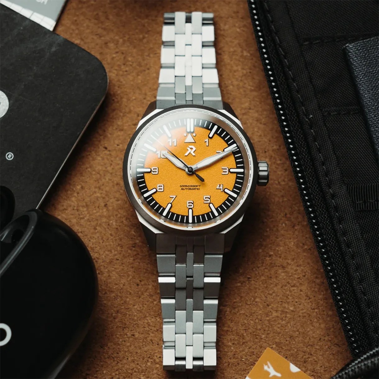 Stainless steel wristwatch with an orange textured dial and black outer ring on a brown surface.