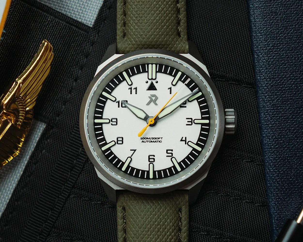Watch with a white dial, black hour markers, yellow second hand, and green textured strap on a black fabric surface.