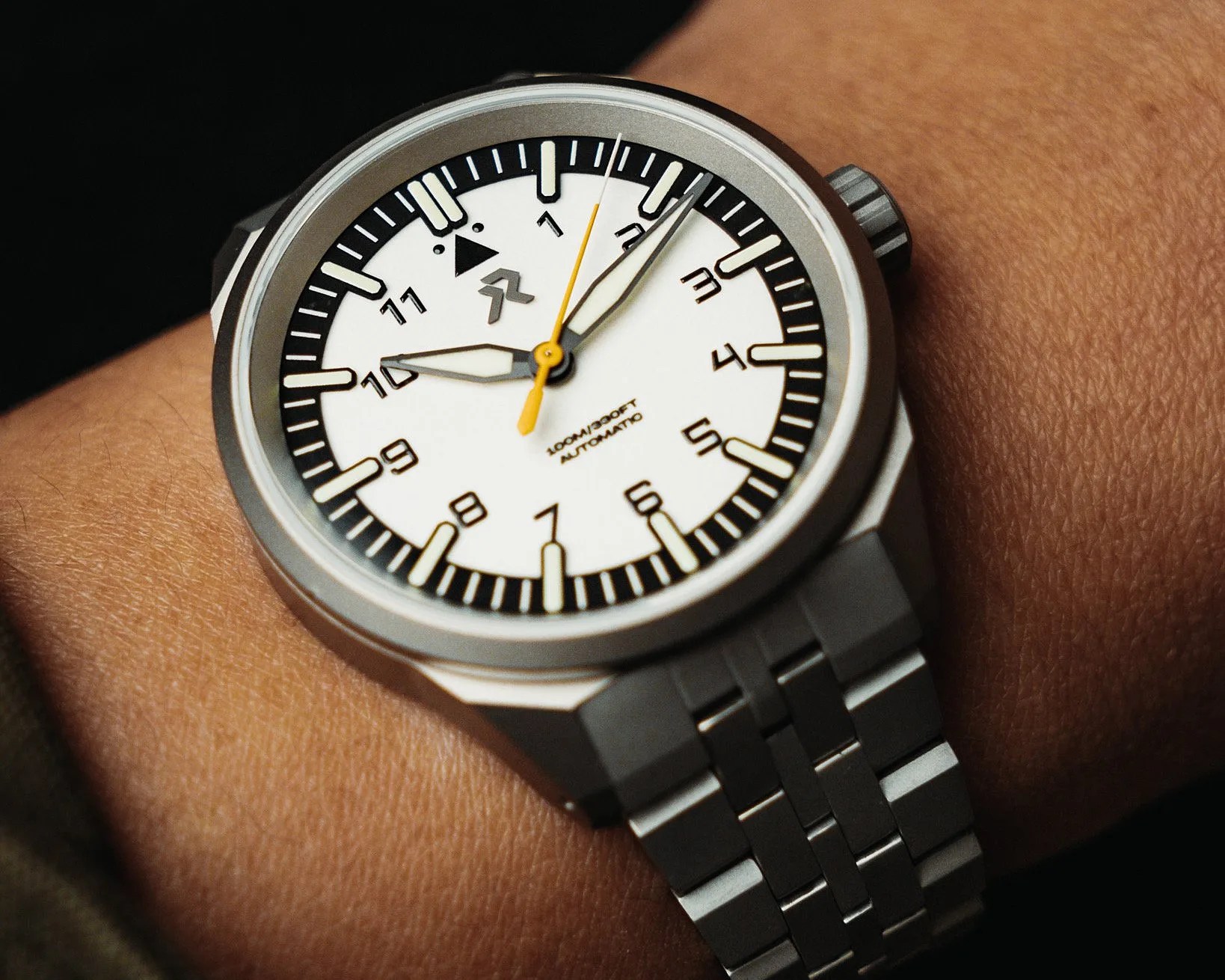 Silver metal wristwatch with white dial, black hour markers, and yellow second hand on a wrist.