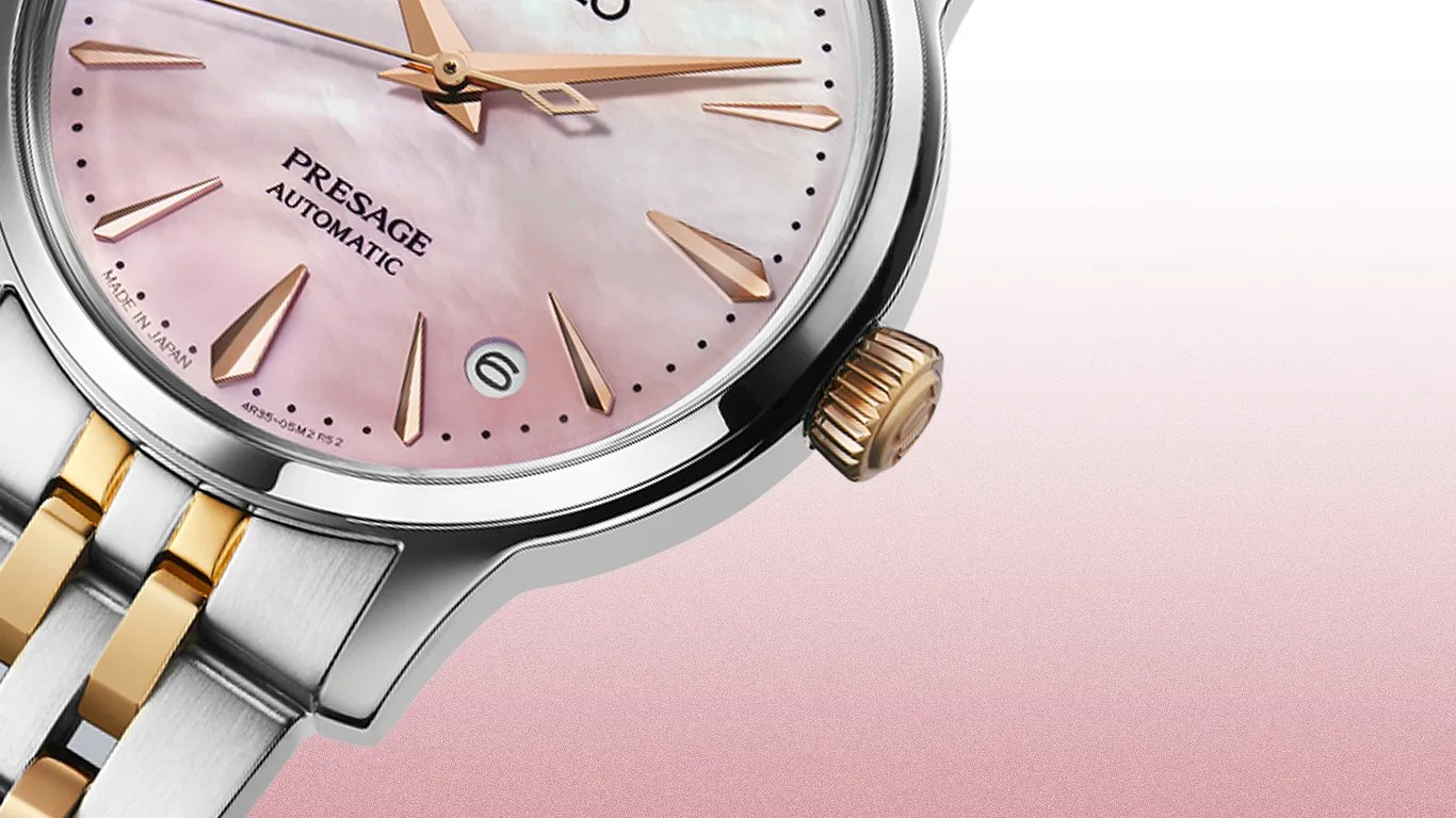 Close-up of a silver and gold wristwatch with a pink mother-of-pearl dial and gold hour markers and hands.