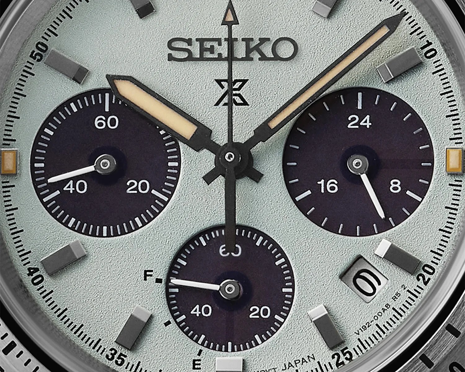 Close-up of a Seiko watch face with light textured background, three black subdials, and luminous hands.