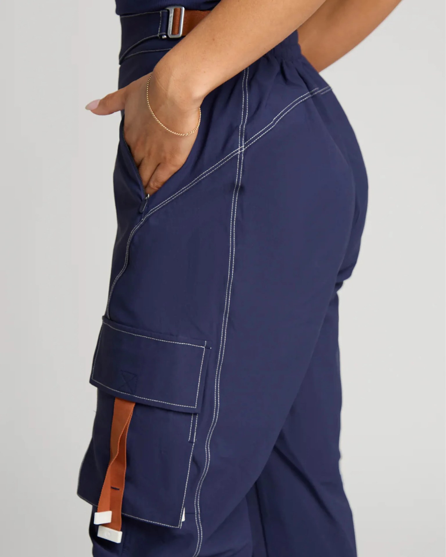 Navy blue cargo pants with white contrast stitching and a brown strap detail on the side pocket.