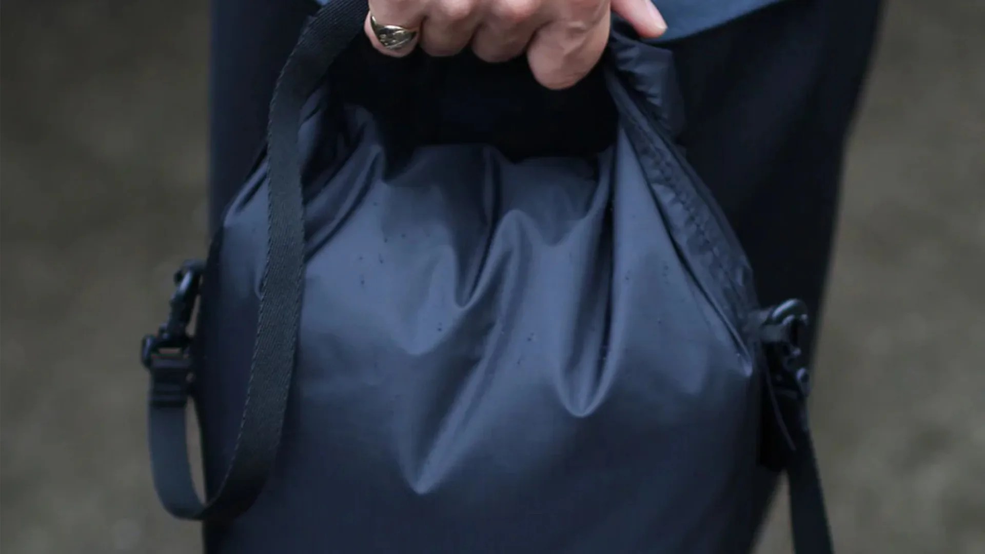 Black waterproof bag with adjustable strap held in a hand.