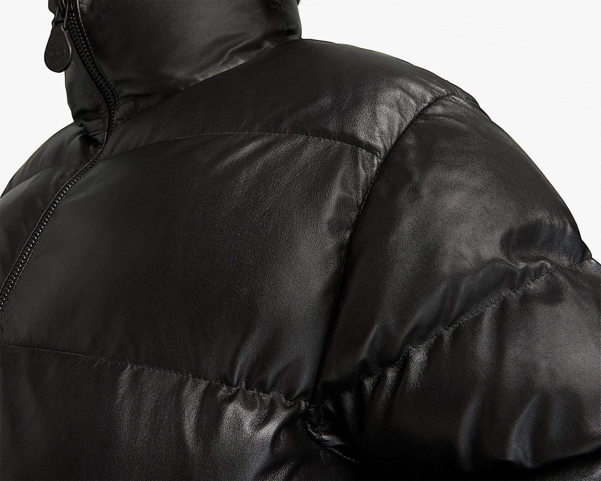 Close-up of a black shiny puffer jacket with a zipper and padded stitching on the shoulder and chest.
