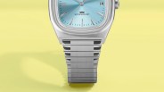 Silver metal wristwatch with a light blue dial and date display on a yellow background.
