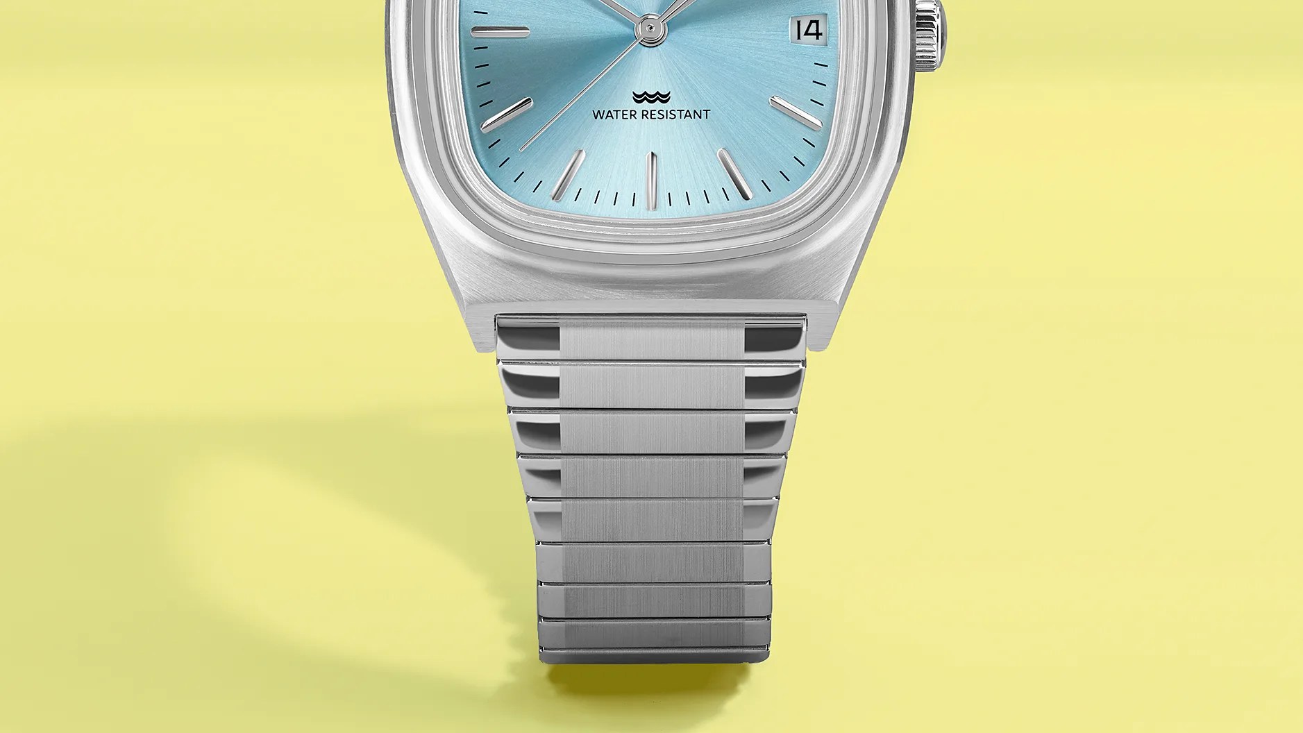 Silver metal wristwatch with a light blue dial and date display on a yellow background.