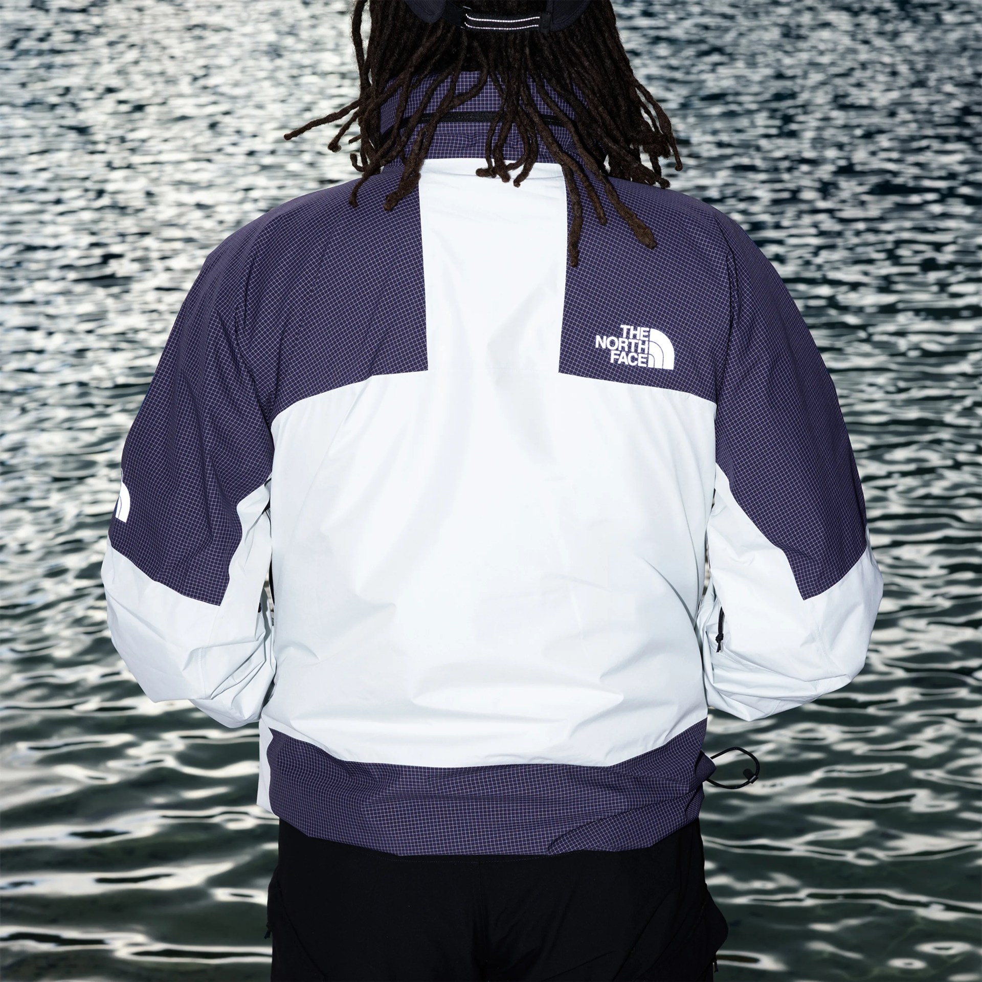 White and dark purple The North Face jacket with grid pattern on upper back and sleeves, worn by a person near water.