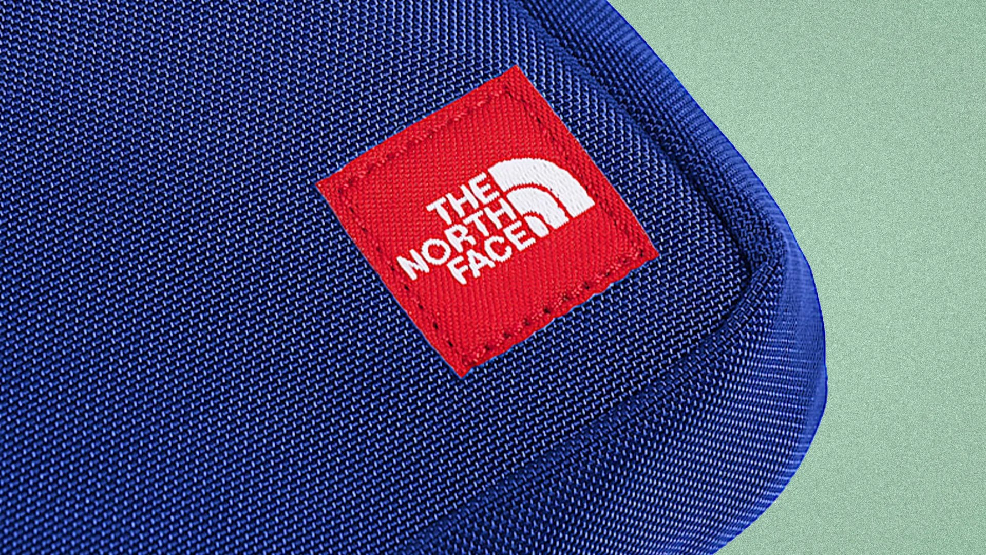 Close-up of a blue fabric item with a red square patch featuring The North Face logo in white.