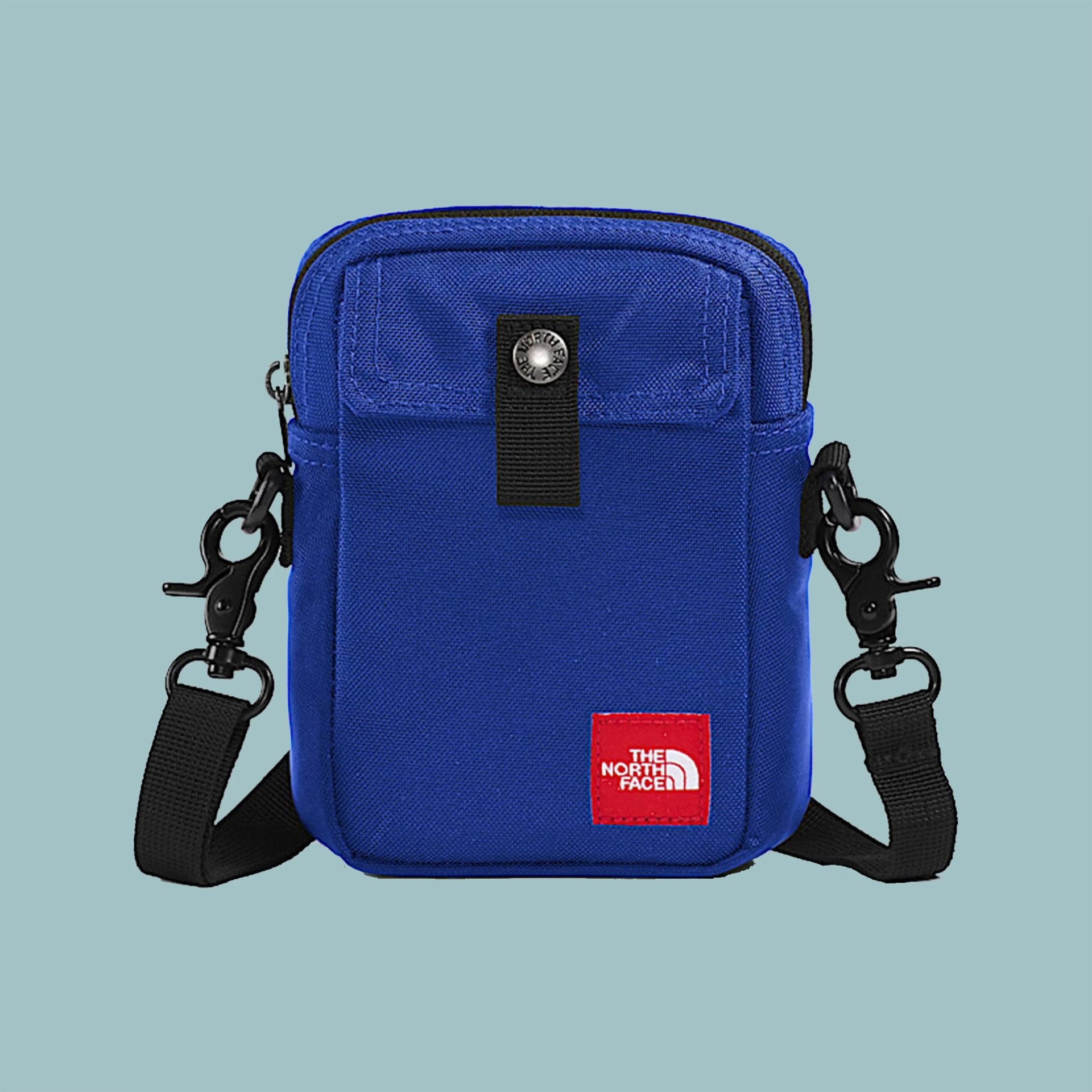 Blue rectangular crossbody bag with black strap and red The North Face logo patch.