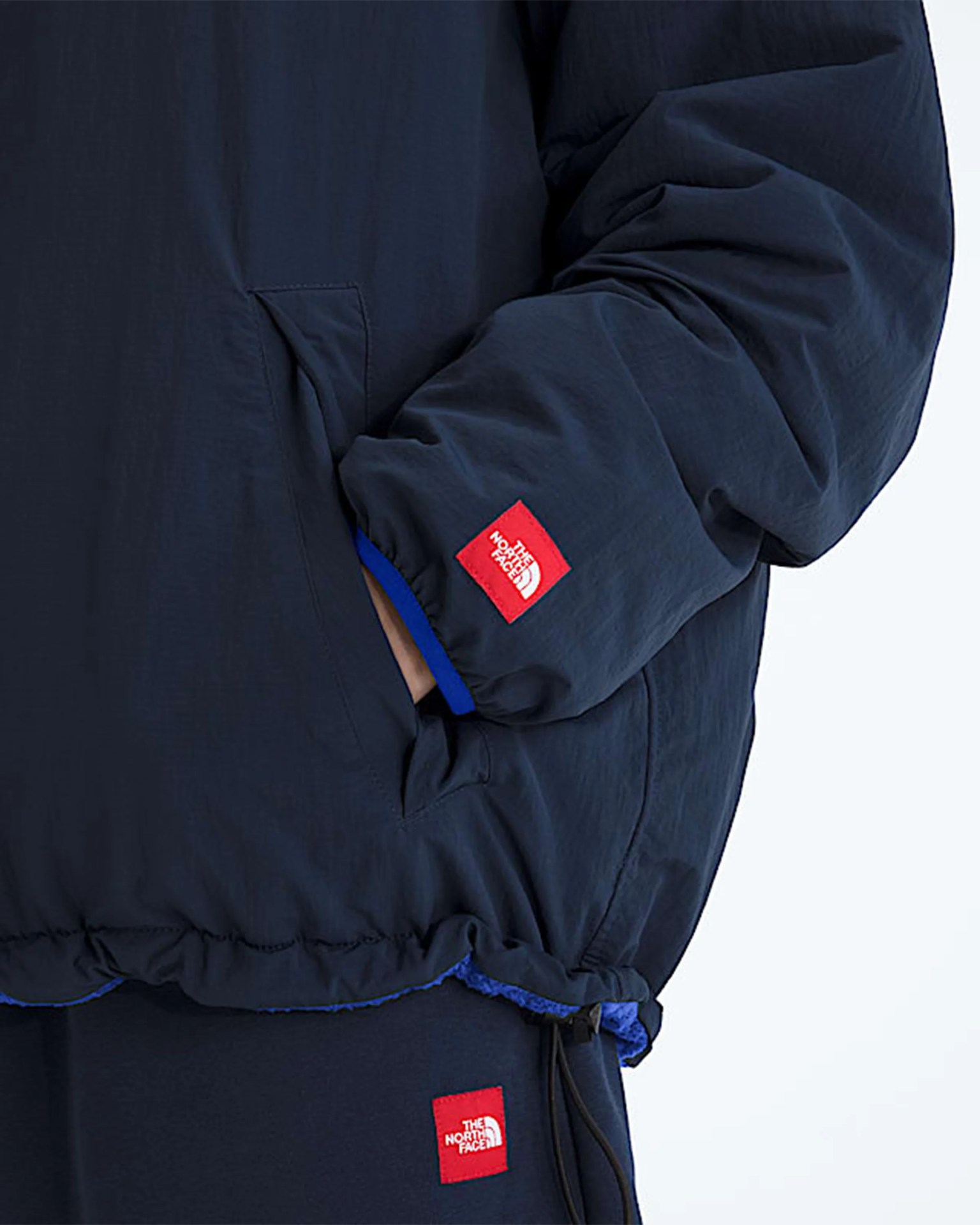 Navy blue jacket and pants with red The North Face logo patches, jacket sleeve partially covering hand.