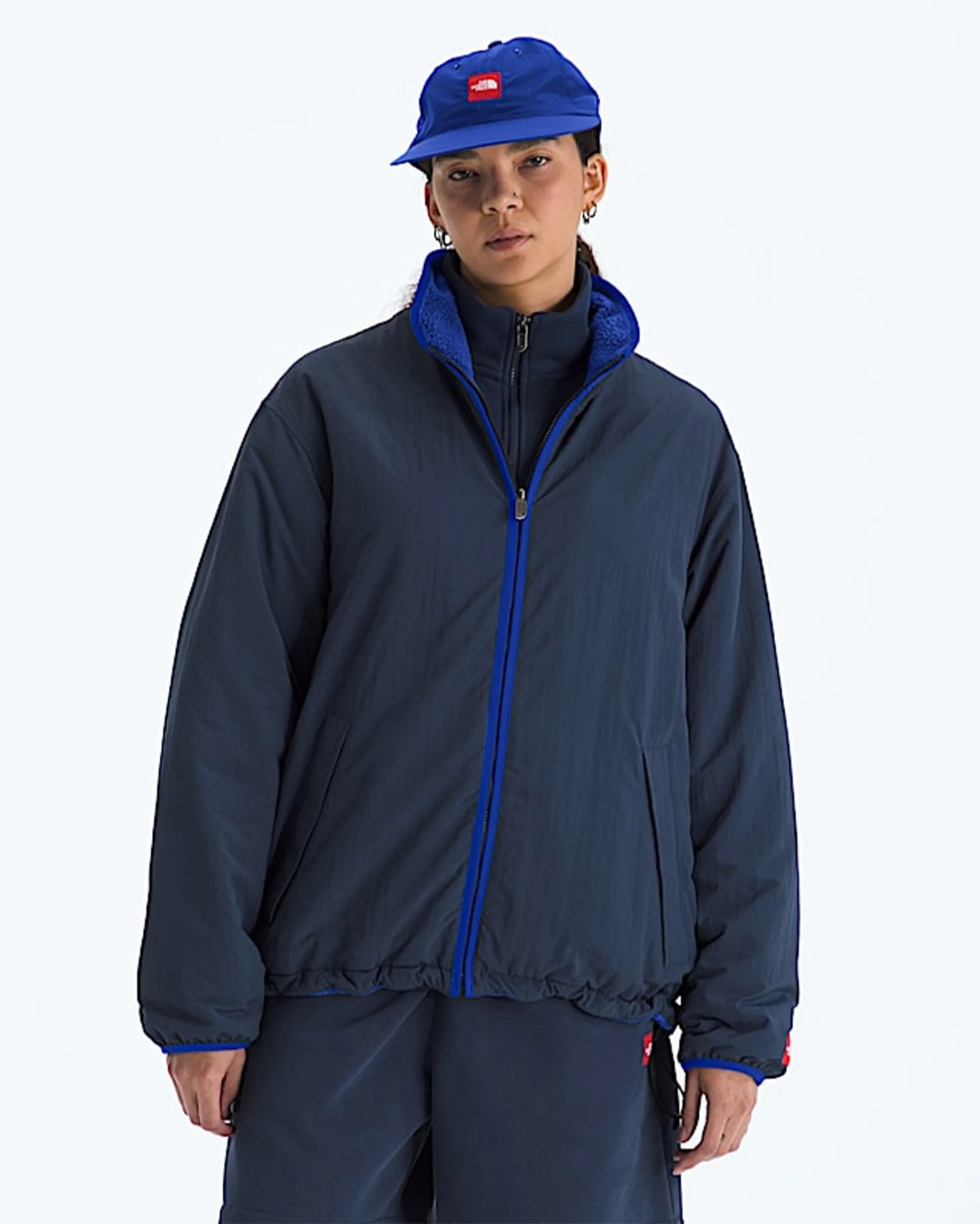 Navy blue zip-up jacket with bright blue trim worn by a person also wearing a matching blue cap.