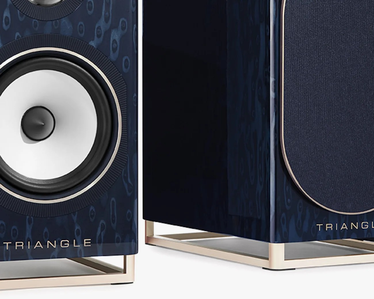 Close-up of two navy blue Triangle speakers with white cones and gold metal stands.