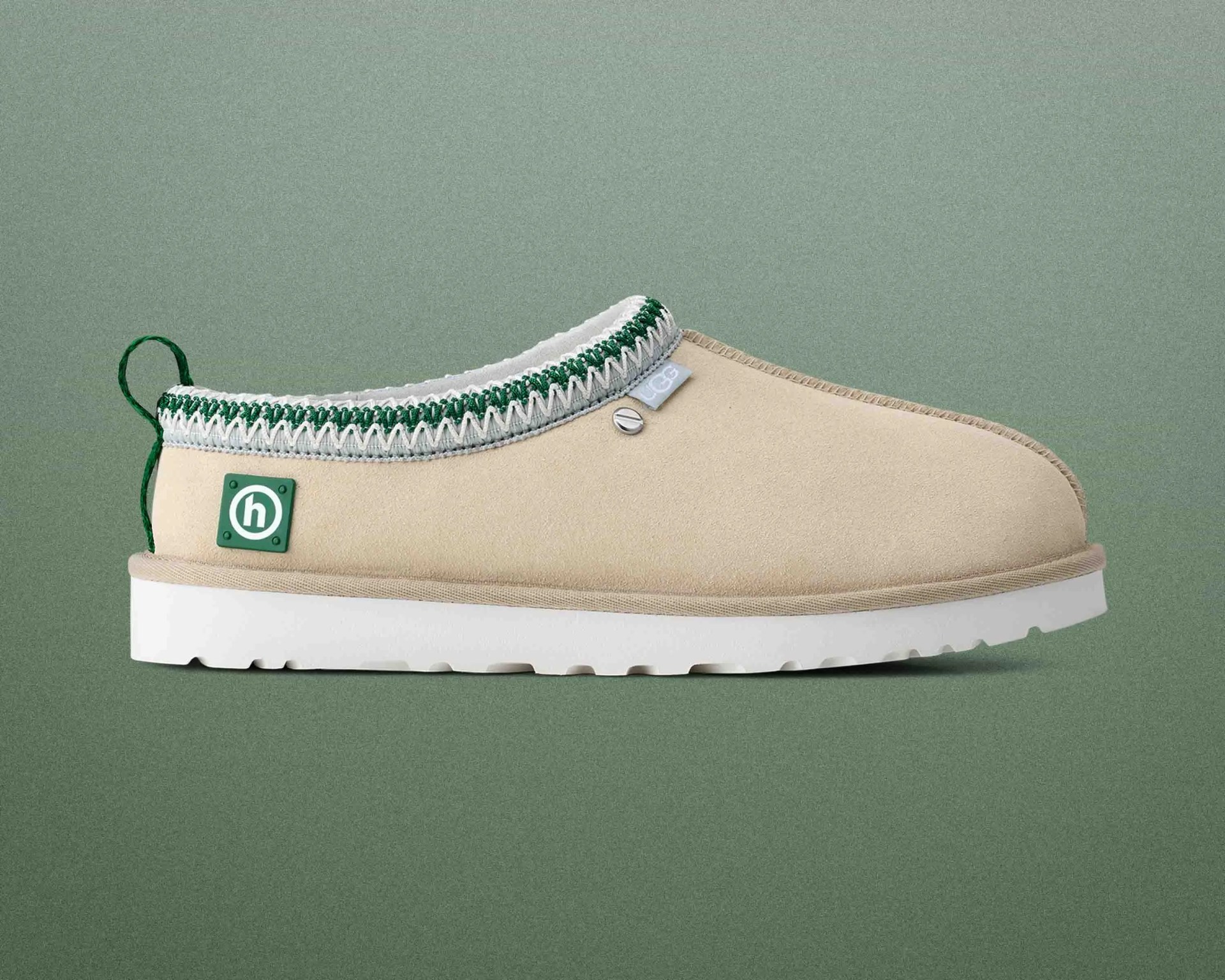 Beige slip-on shoe with white sole, green and white trim, and green pull tab on a green background.