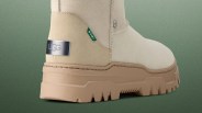 Beige suede UGG boot with thick tan rubber sole and metal UGG logo plate on the heel.