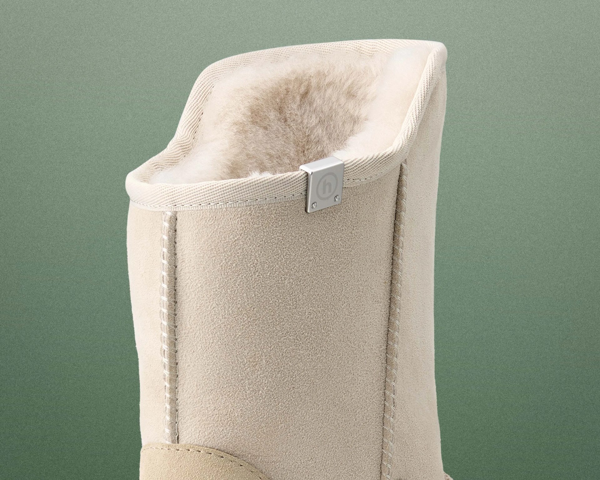 Close-up of the top part of a beige suede boot with soft, fluffy lining and a small metal tag with an "h" logo.