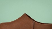 Close-up of the upper part of a brown suede shoe against a light green background.