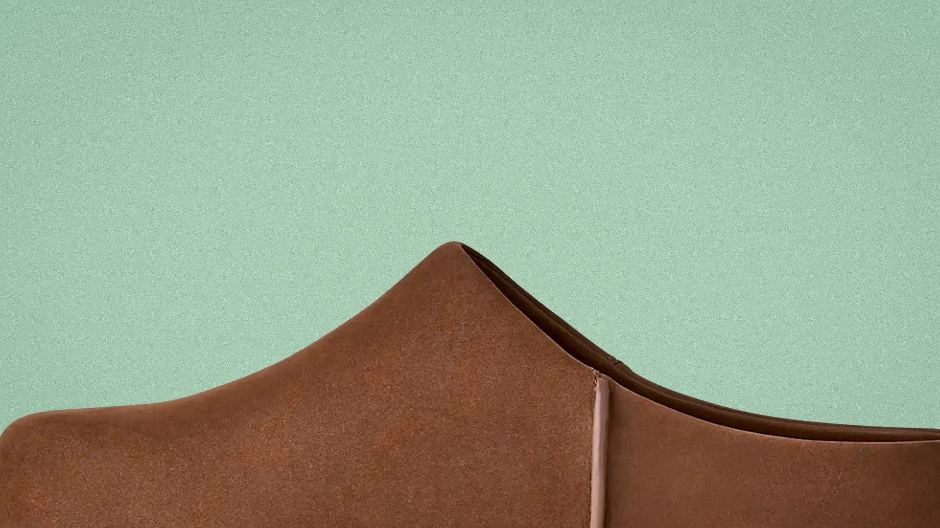 Close-up of the upper part of a brown suede shoe against a light green background.
