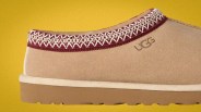 Close-up of a tan suede UGG slipper with maroon and white stitched trim and a brown rubber sole.