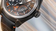 Close-up of a black watch with visible gears, orange accents, and a black leather strap with orange stitching.