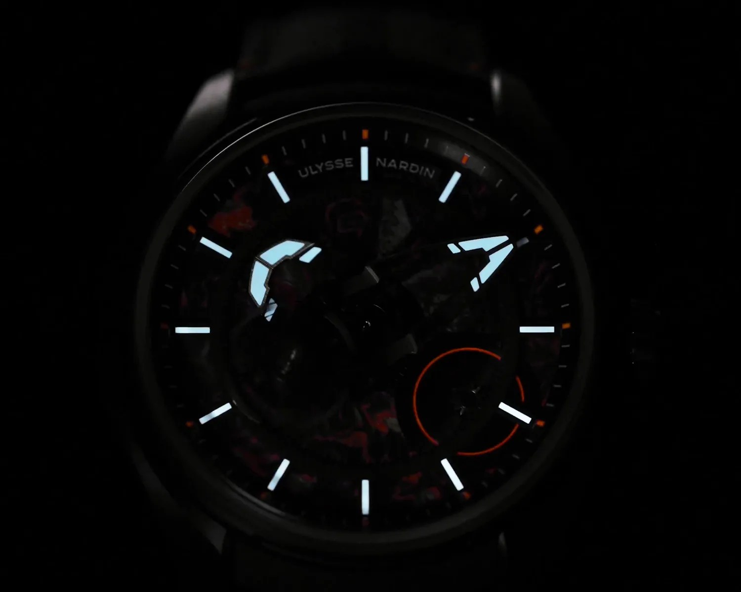 Dark watch face with luminous hour markers and hands, featuring the brand name "Ulysse Nardin" near the top.