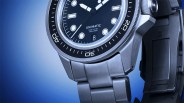 Close-up of a stainless steel Unimatic dive watch with black dial and rotating bezel on a blue gradient background.