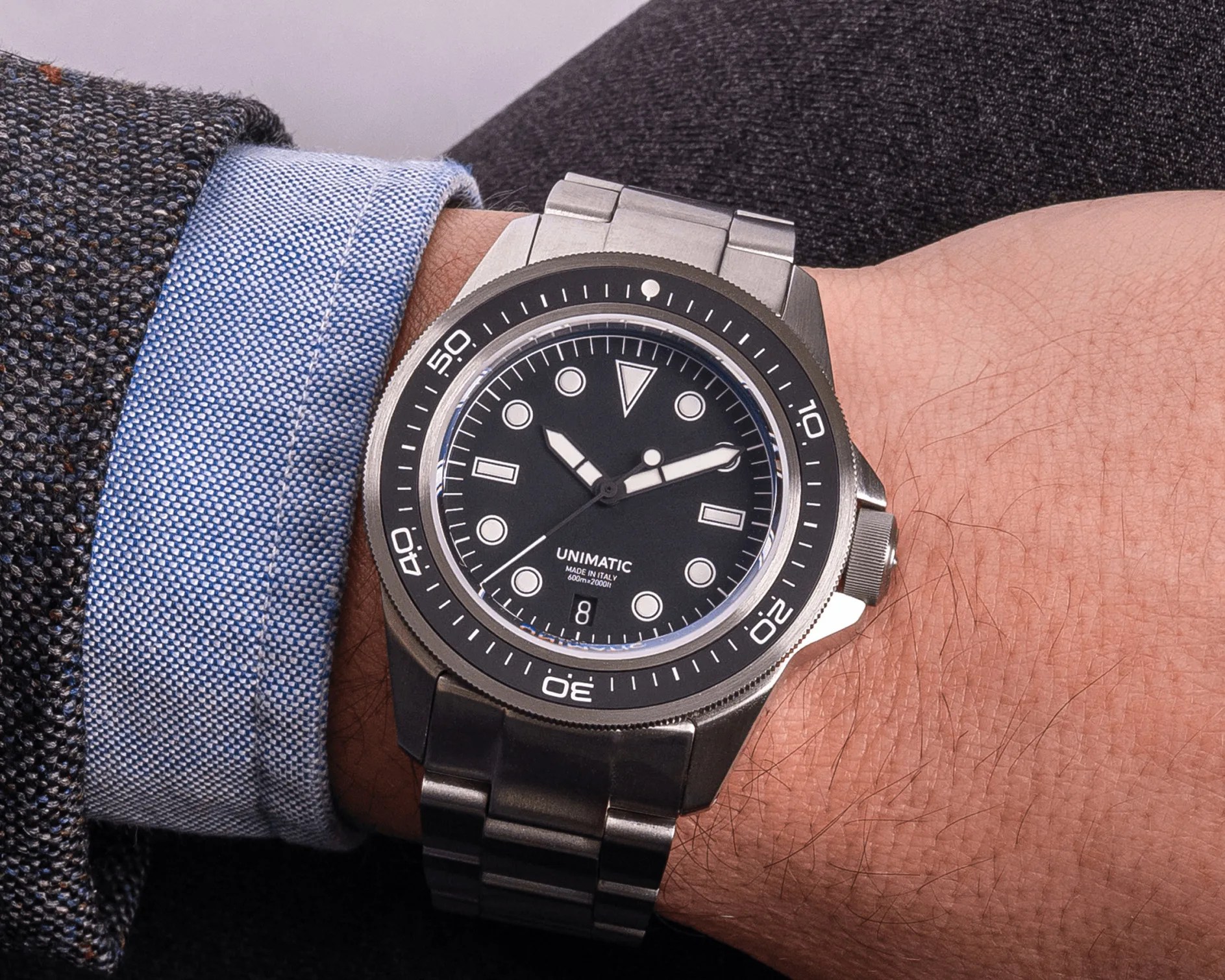 Stainless steel Unimatic wristwatch with black dial and luminous markers on a wrist.