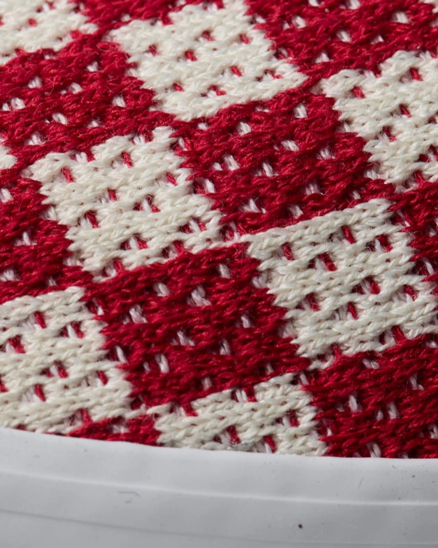 Close-up of red and white knitted fabric with a geometric pattern and a white rubber edge.