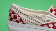 Close-up of a cream and red checkered knit Vans slip-on shoe with a white rubber sole against a green background.