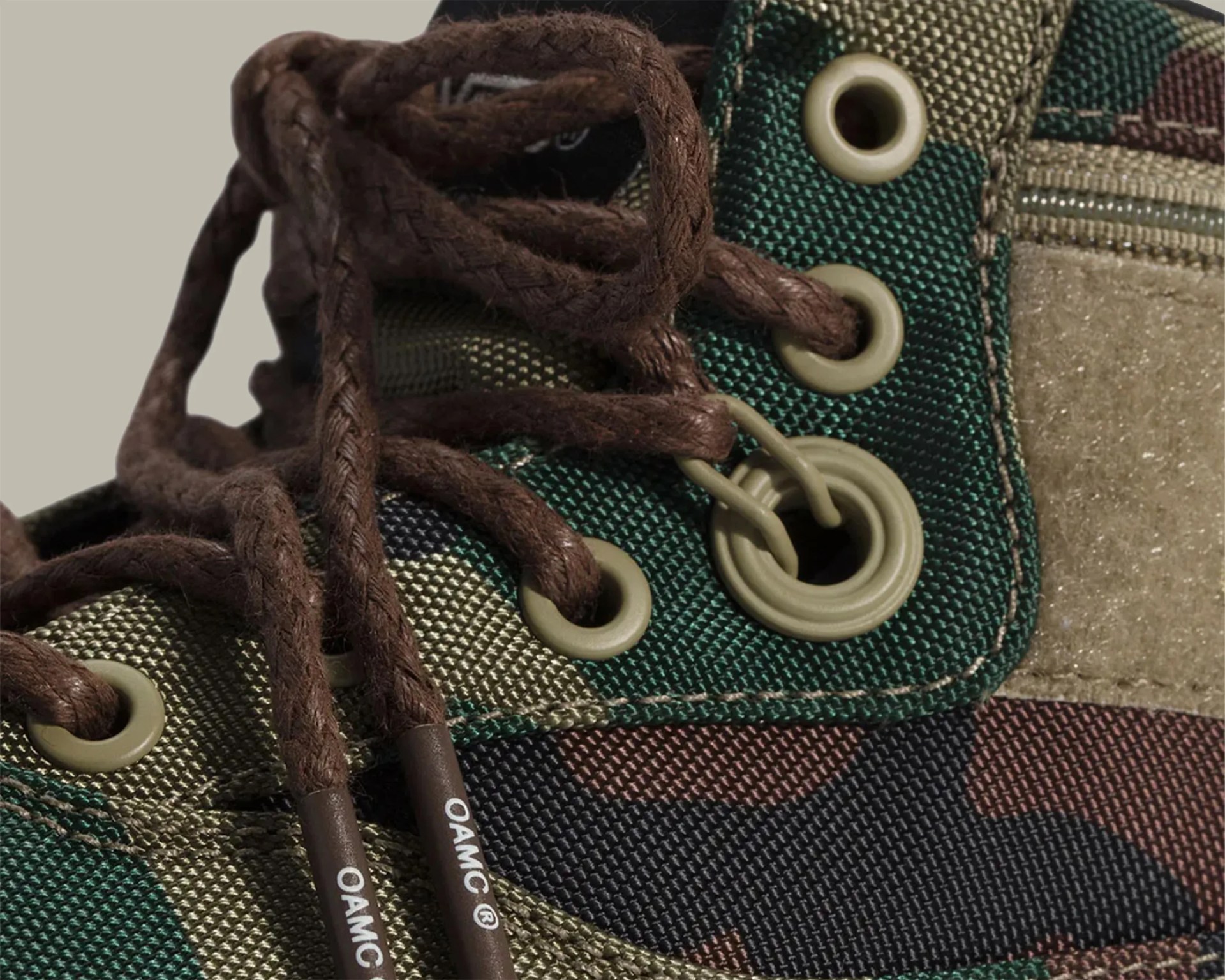 Close-up of a camouflage fabric shoe with brown laces threaded through olive green metal eyelets.