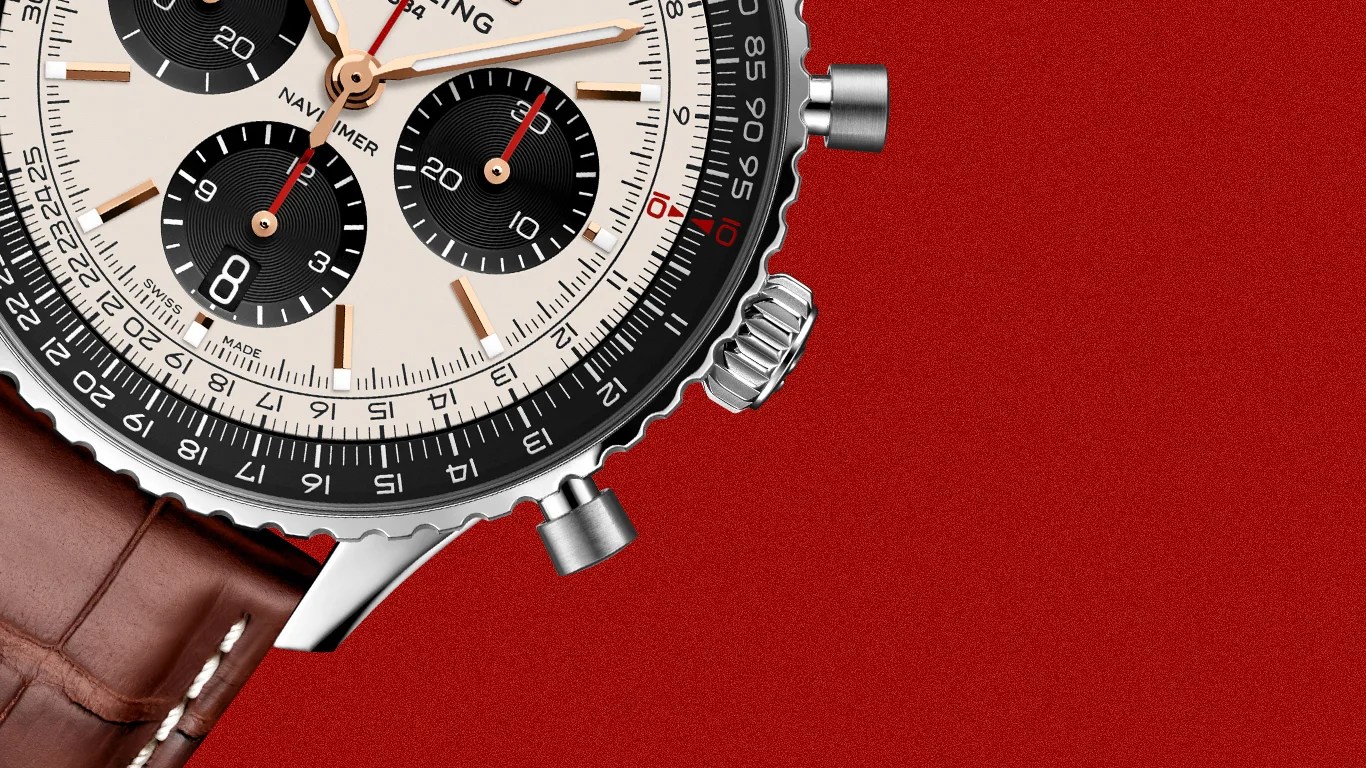 Close-up of a silver chronograph watch with a white dial, black subdials, red second hands, and a brown leather strap on a red background.