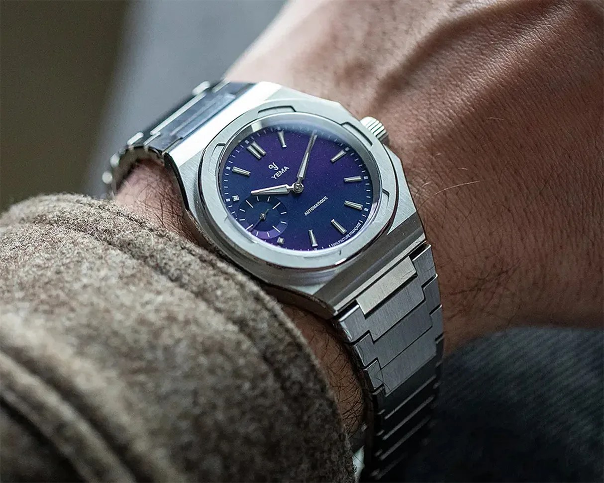 Stainless steel wristwatch with a blue dial and silver hour markers worn on a wrist.