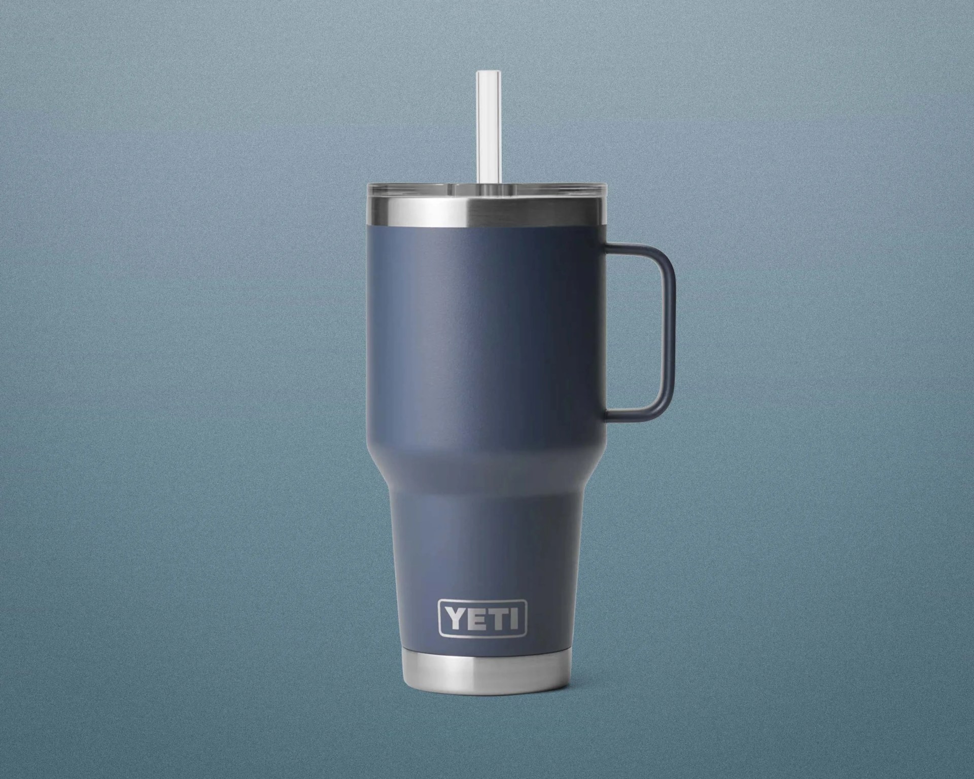 Matte navy blue YETI tumbler with handle, clear lid, and clear straw on a blue gradient background.