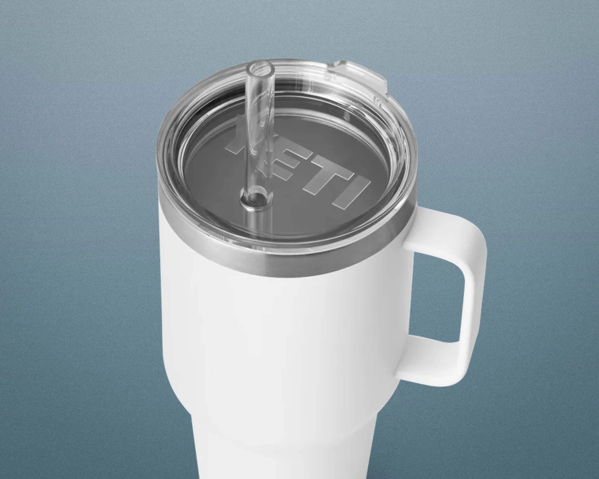 White insulated YETI tumbler with handle and clear lid with straw on a blue-gray background.