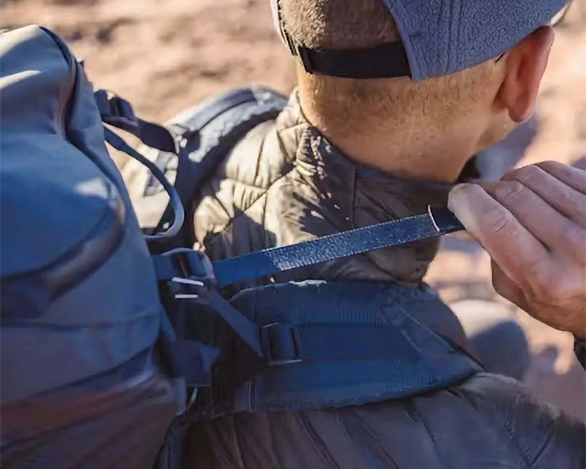 Close-up of a person adjusting the strap of a dark blue backpack worn over a quilted jacket and a blue cap.