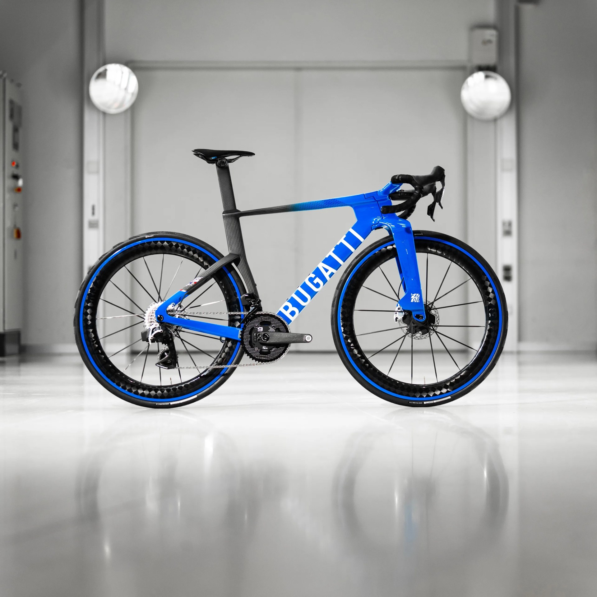 Blue and black Bugatti road bike with carbon frame and deep-section wheels on a glossy floor.