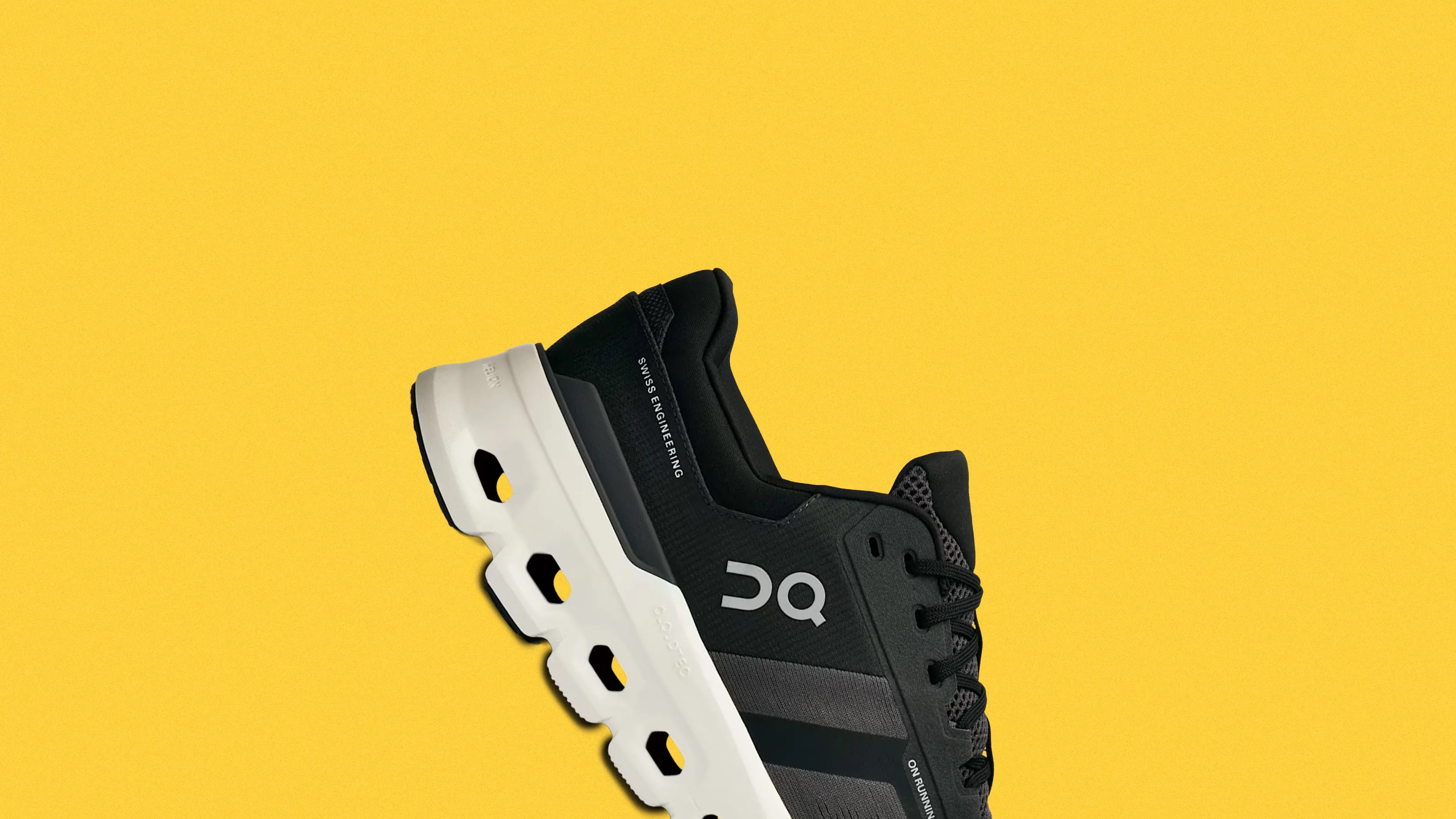 Black and gray On Running sneaker with white sole featuring hollowed-out sections, against a yellow background.