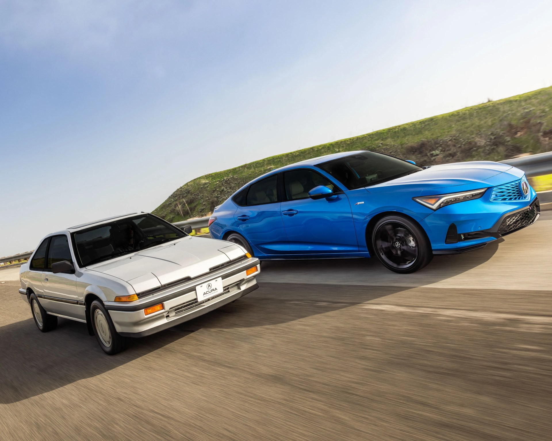 Silver vintage Acura Integra coupe and blue modern Acura Integra sedan driving side by side on a highway.