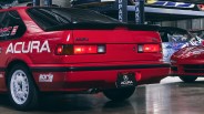 Red Acura Integra RS hatchback with black rear spoiler and white Borla Exhaust decal in a garage.